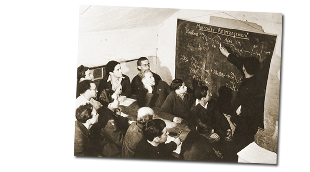 Un cours de Dr. Michaelis pour les internés du Camp I (Île-aux-Noix, Québec. Il écrit au tableau noir des équations sous l’œil attentif des étudiants.